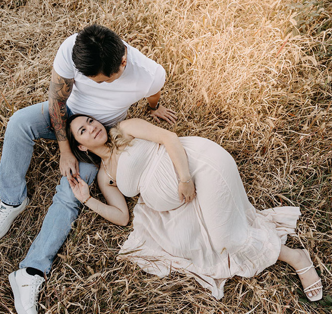Pregnant woman laying on a field with her head placed on her partners lap