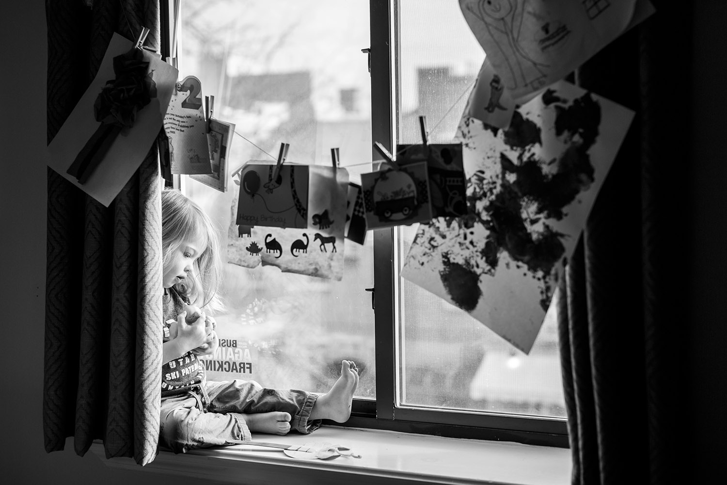 BW toddler holding a toy while sitting on the windowsill