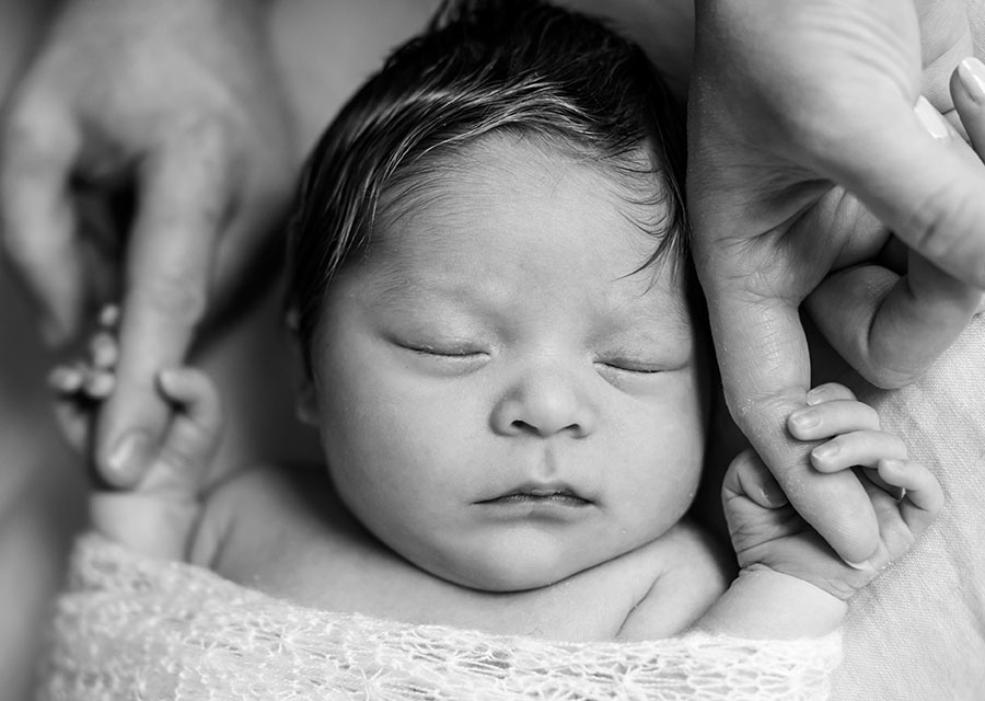 Sleeping newborn baby holding its parents fingers