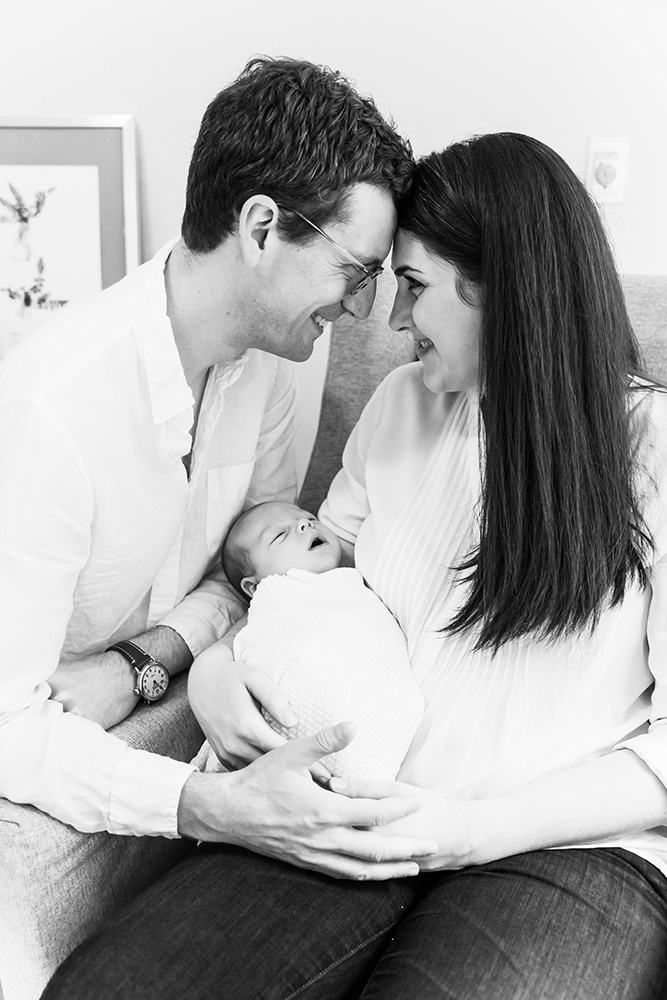 BW Parents smiling at each other head to head while holding their newborn baby