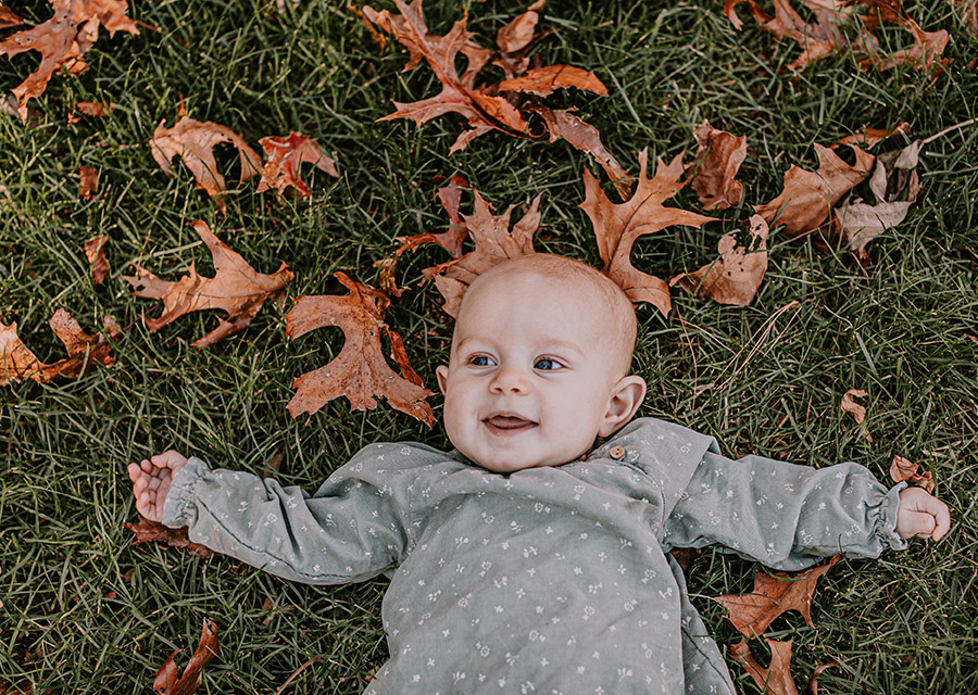 Baby girl laying in the grass with leafs around her