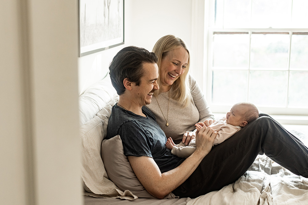 Parents sitting on a bend smiling at their newborn baby