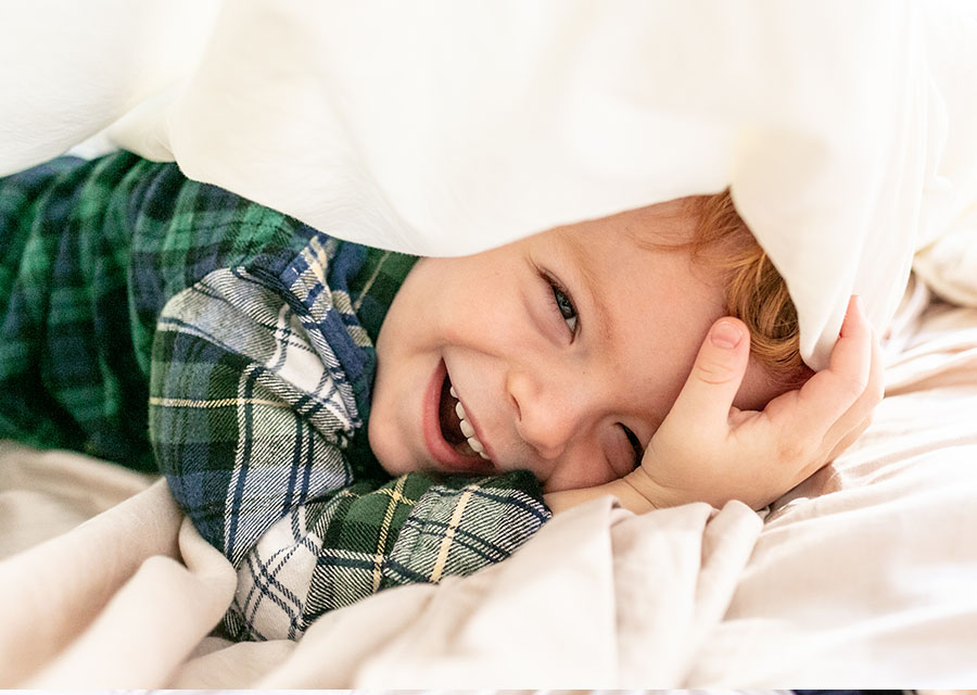 Little boy under a blanket smiling at the camera