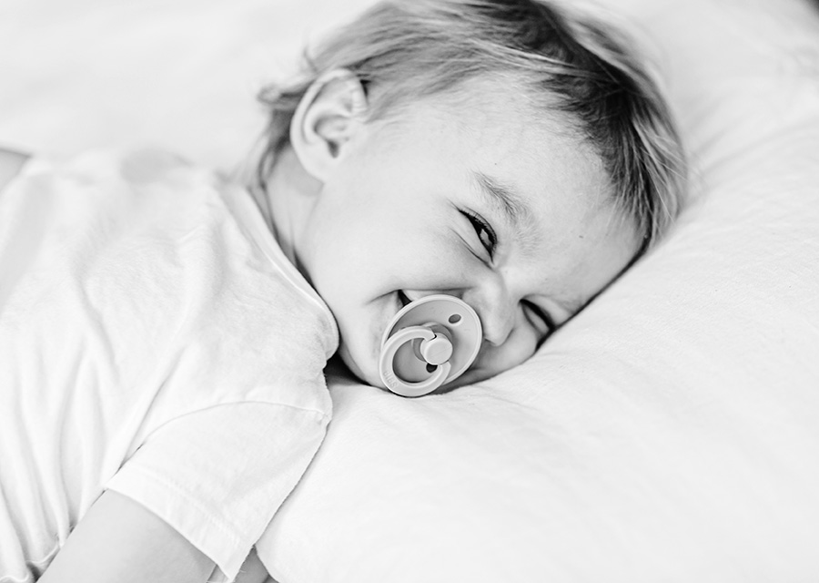 Toddler laying in bed smiling at the camera