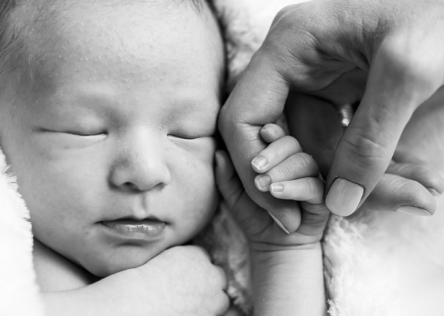 Newborn baby holding his mothers finger in his hand