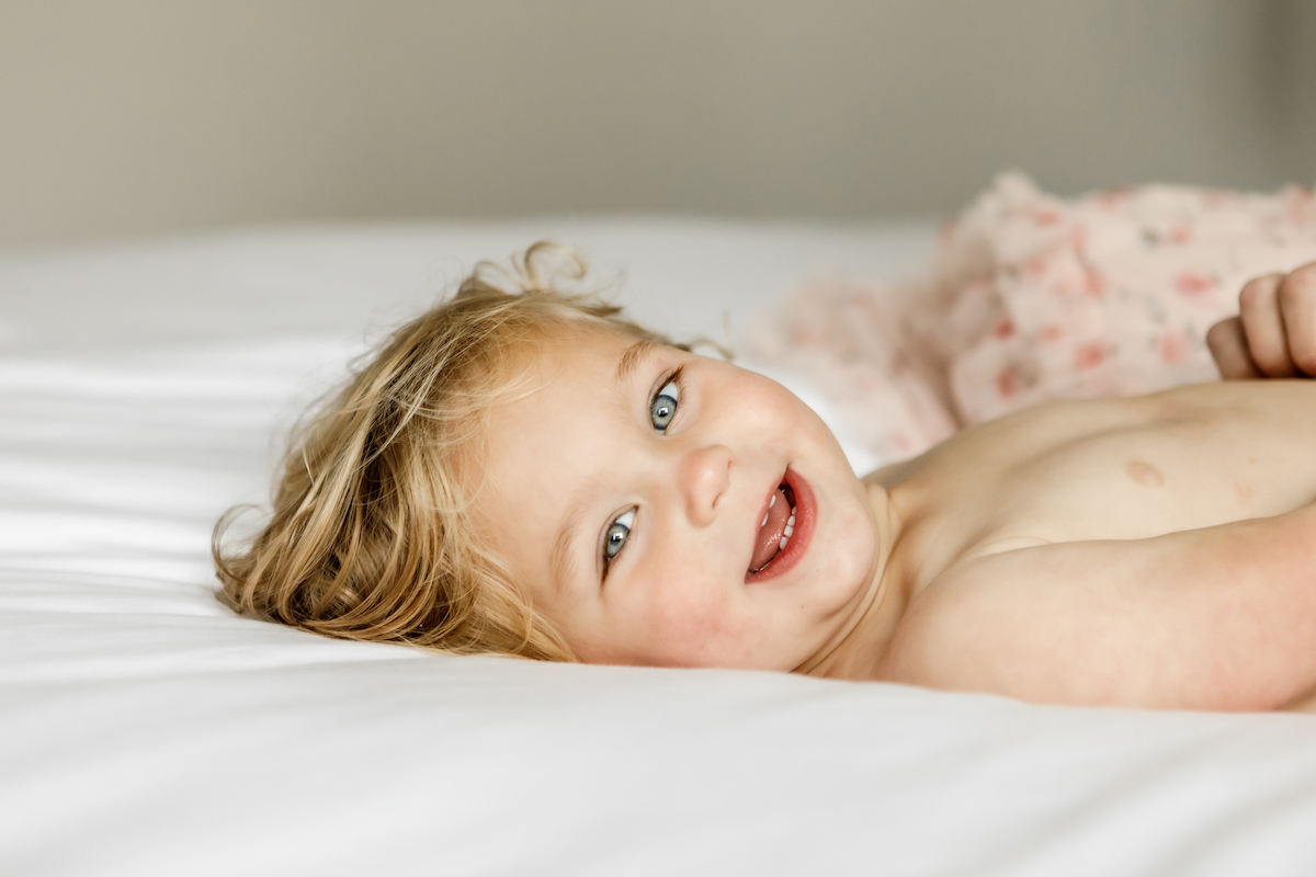 Toddler laying on a bed smiling at the camera
