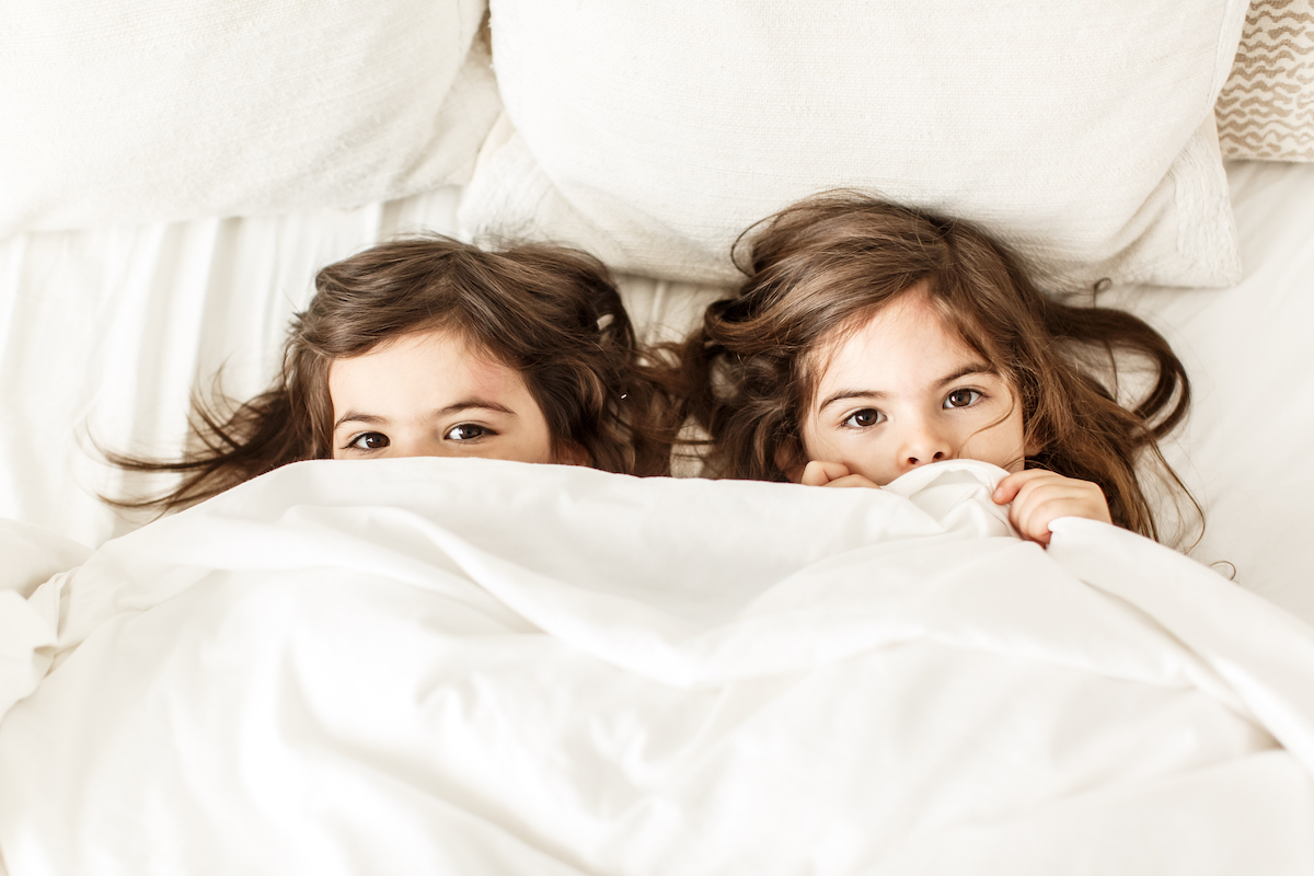 Sisters laying under a blanket with only their eyes showing