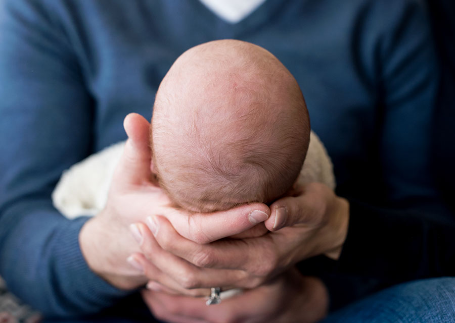 Newborn baby's head held by its dad's hands