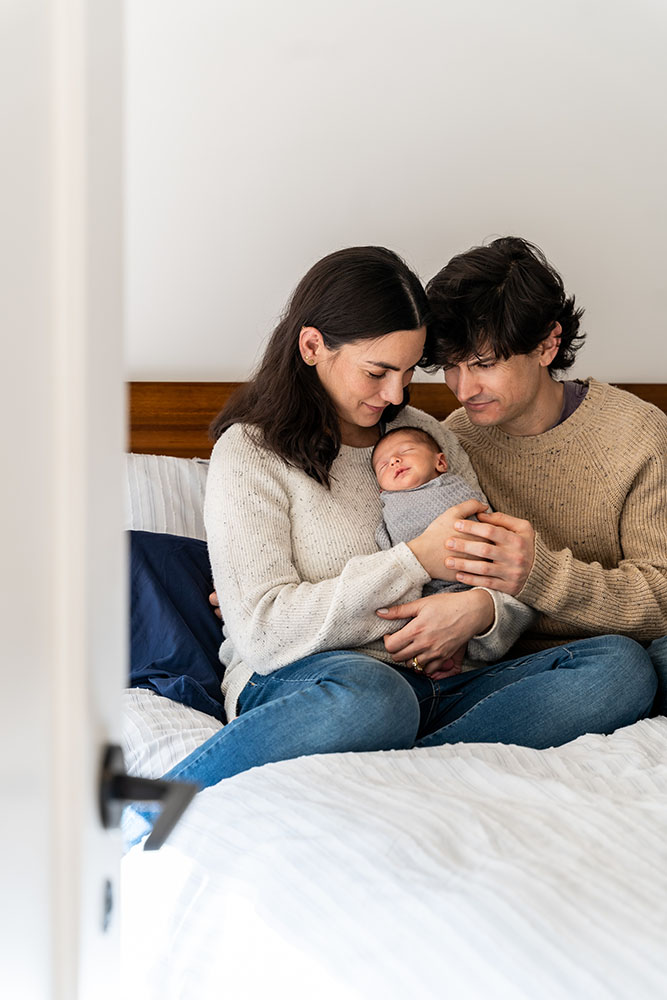 Parents holding their newborn baby sitting on a bed