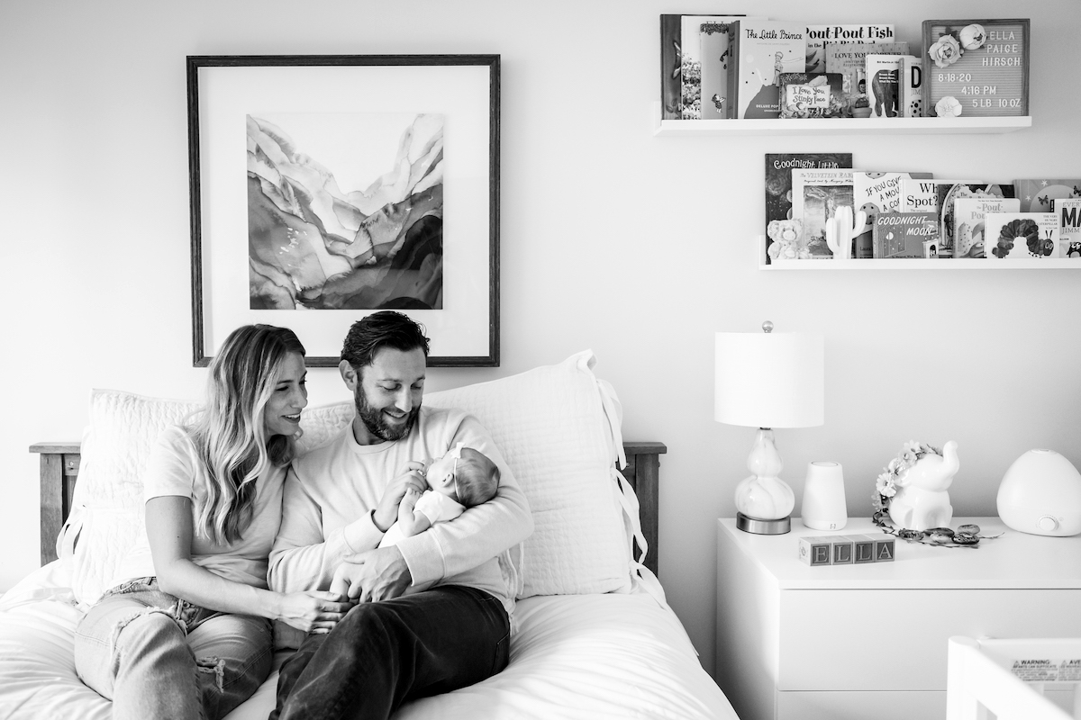 BW Mom and dad sitting on their bed with their newborn baby in dad's arms