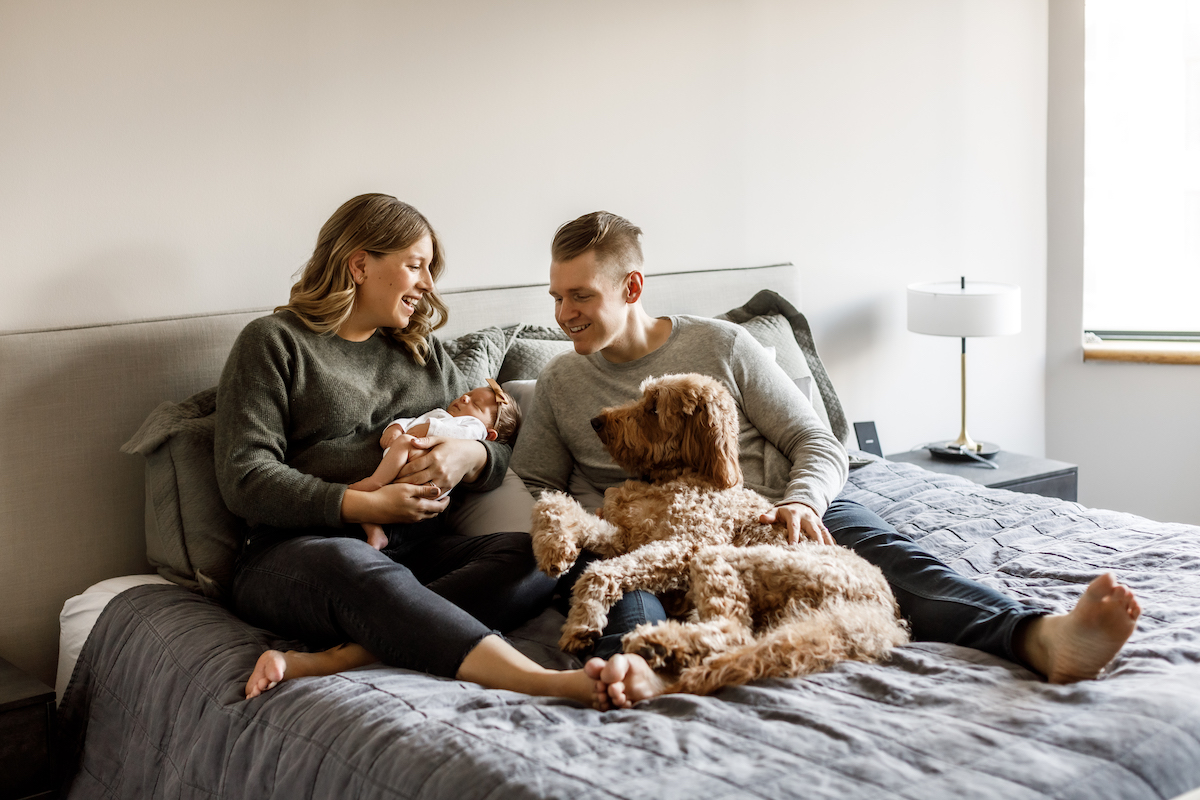 Parents sitting on their bed with their newborn baby and their dog