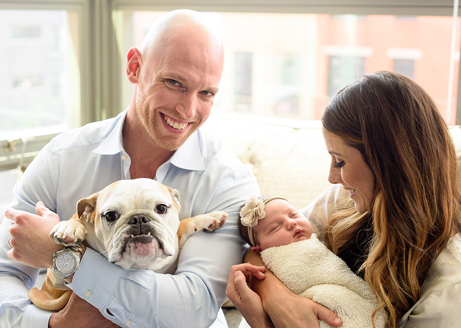 Dad holding the dog and mom holding their newborn baby girl