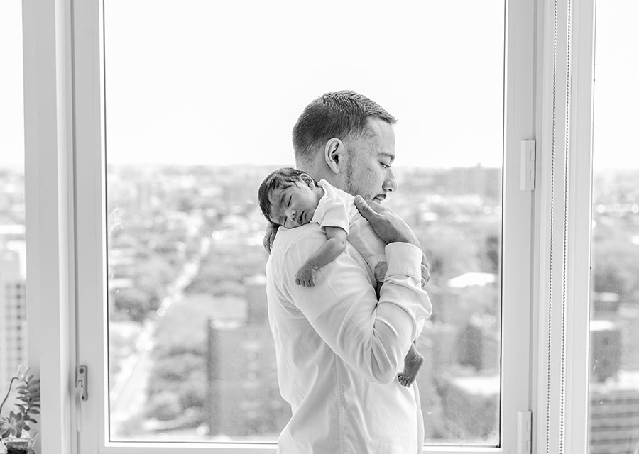 BW Dad holding his sleeping newborn baby in front of window