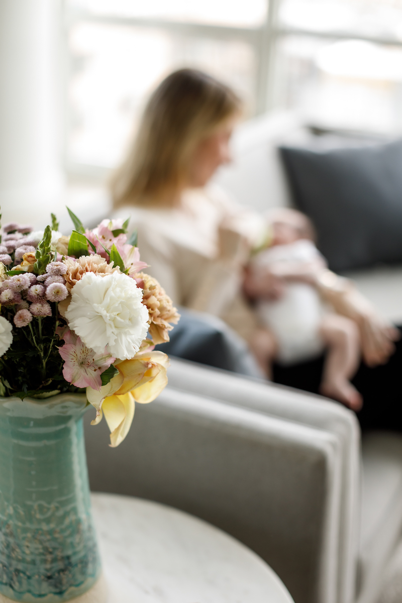 Flowers on a table with mom feeding her baby in the backround