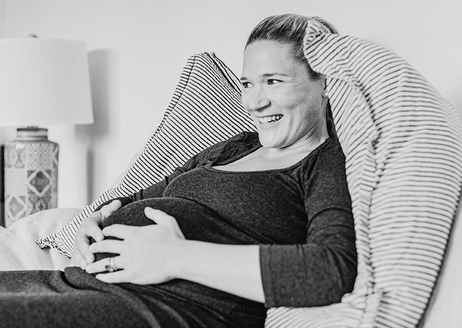 BW Pregnant woman laughing on a bed with her hands on her belly