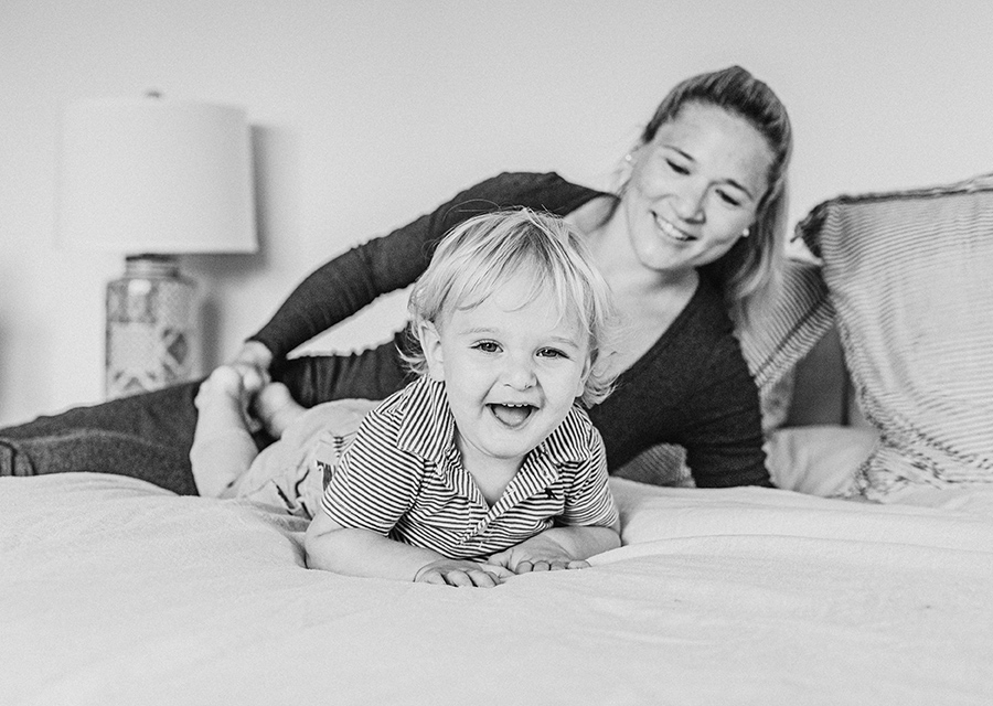 Mom and toddler laughing while laying on a bed