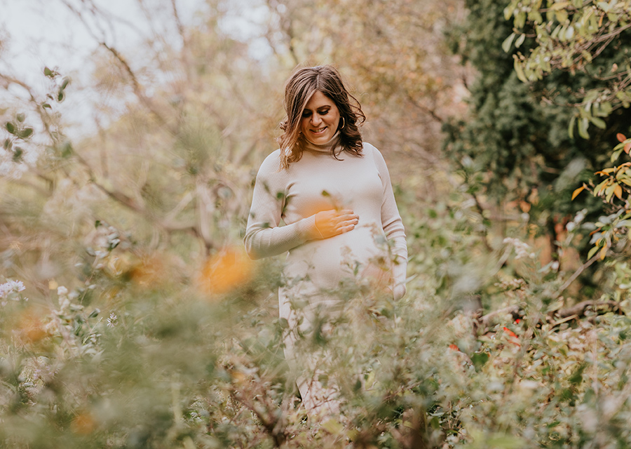 Pregnant woman in a field of flowers smiling down on her belly