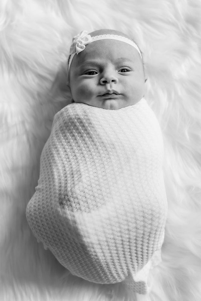 Black and white photo of swaddled newborn baby with head band