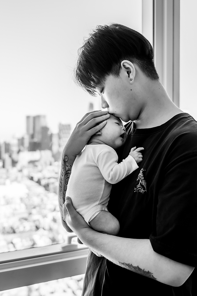 Black and white photo of daddy holding his newborn son with nyc skyline in the background