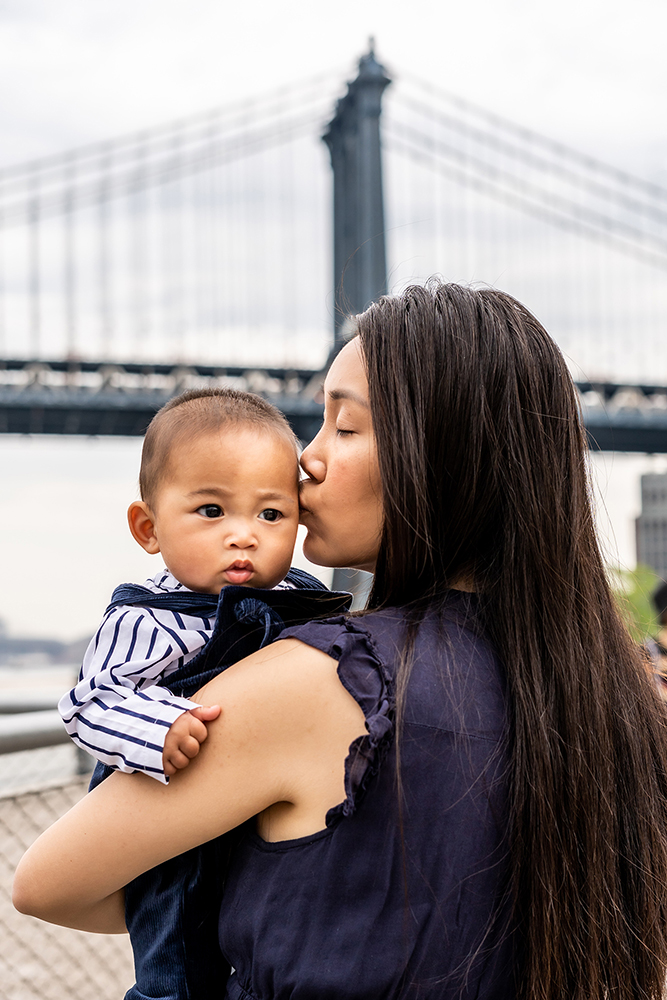 mommy kissing his baby boy in front of manhattan bridge