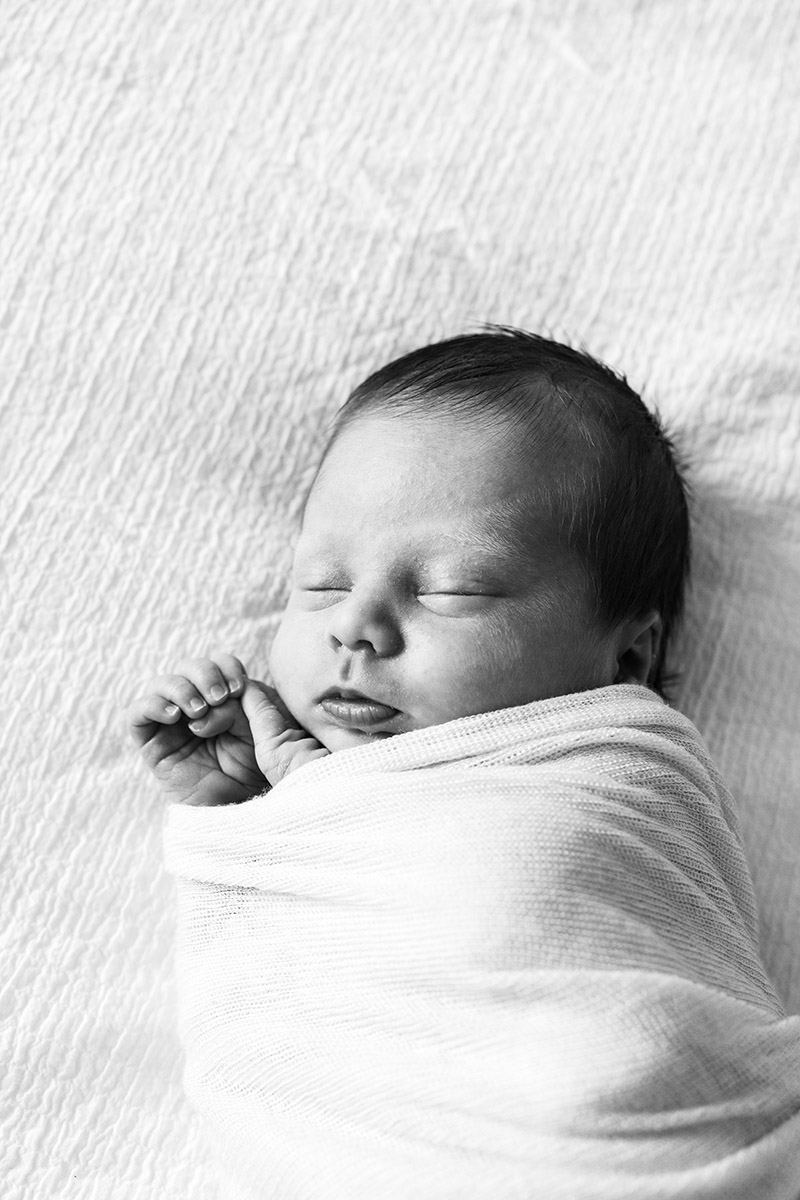 BW portrait of sleeping newborn on white bed sheet