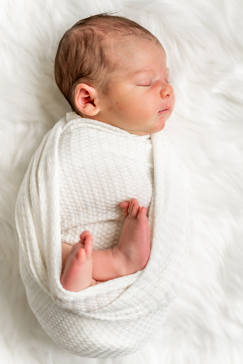 Newborn baby swaddled in white blanket with feet sticking out