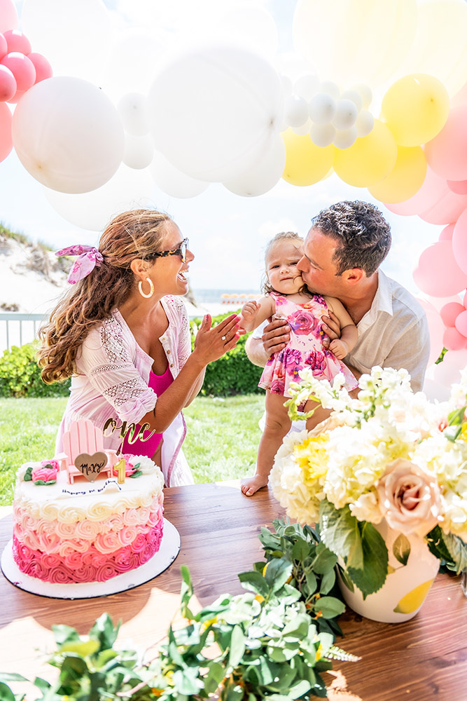 family of three sitting at a table with birthday cake on it, dad kisses his daughter