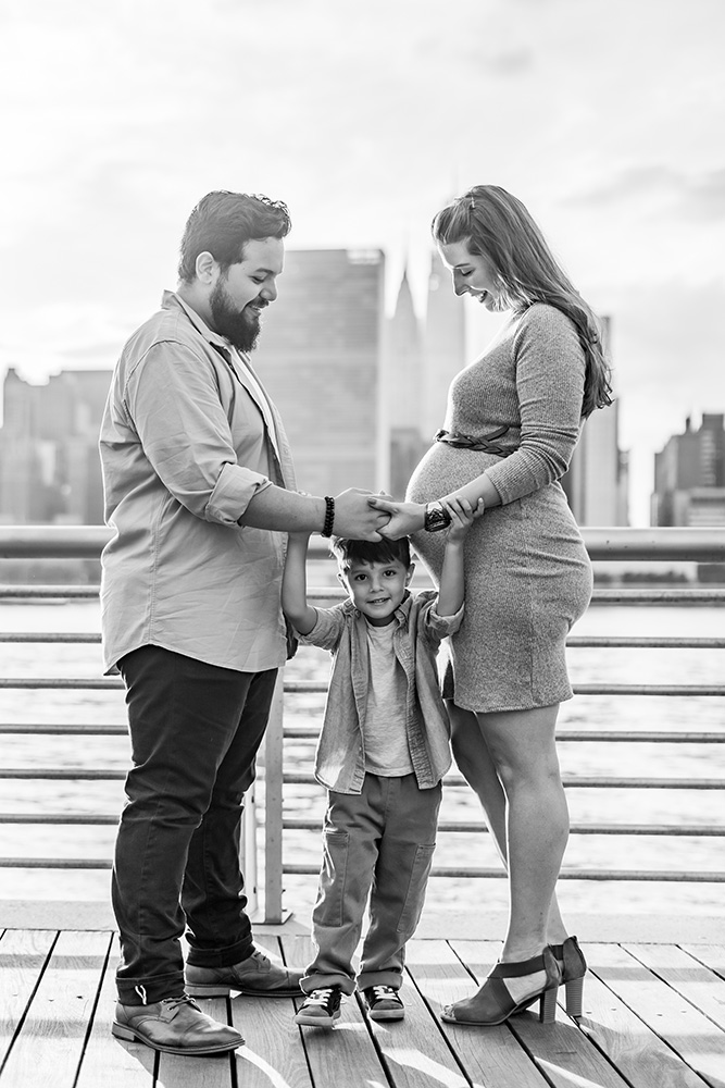 Black and white photo of family with pregnant mom with skyline of Manhattan in the background