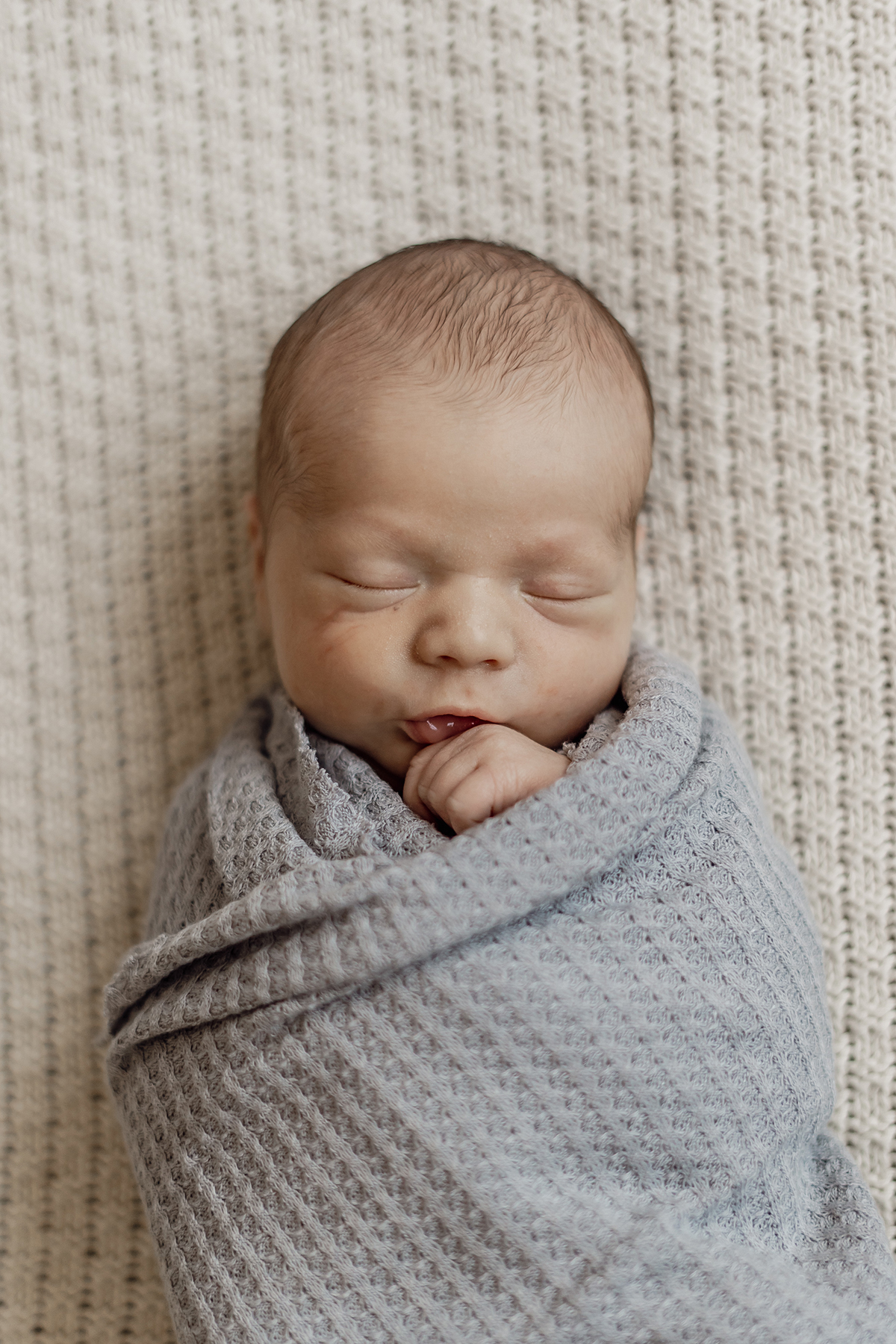 Newborn baby sleeping swaddled in grey blanket