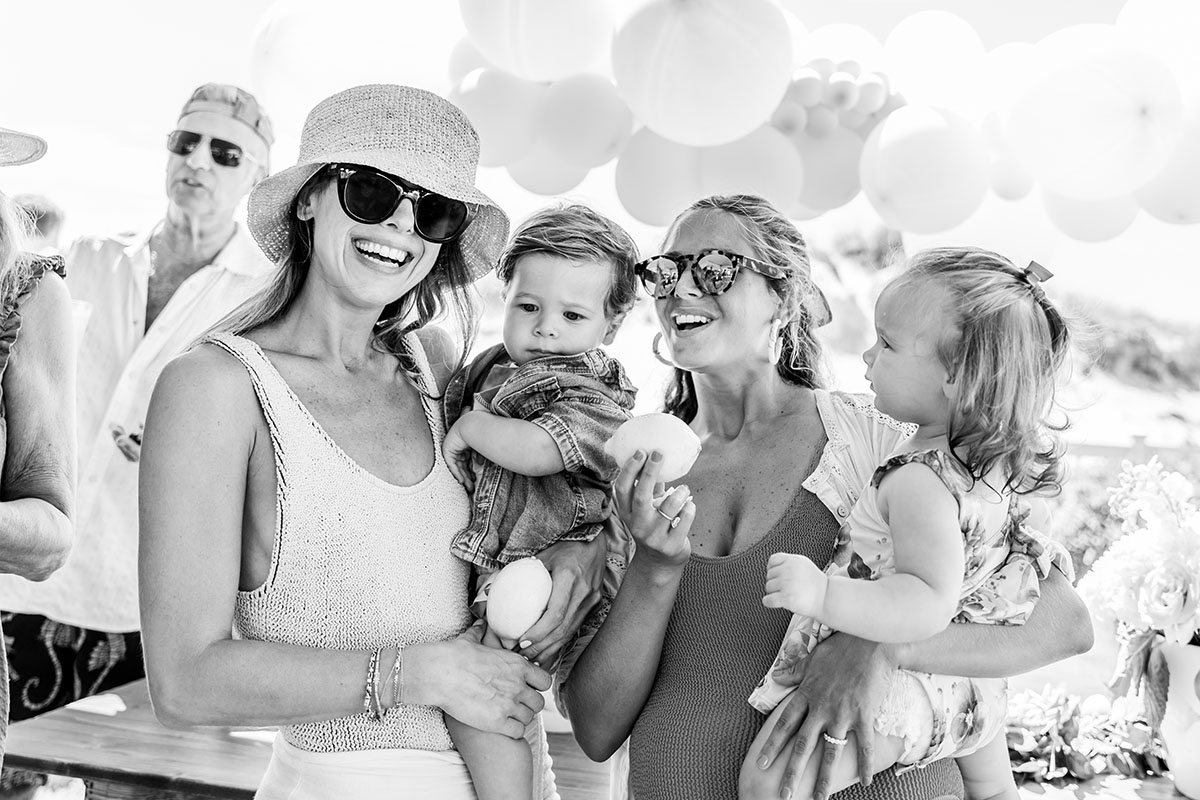 two laughing moms are holding their toddlers on a party black and white