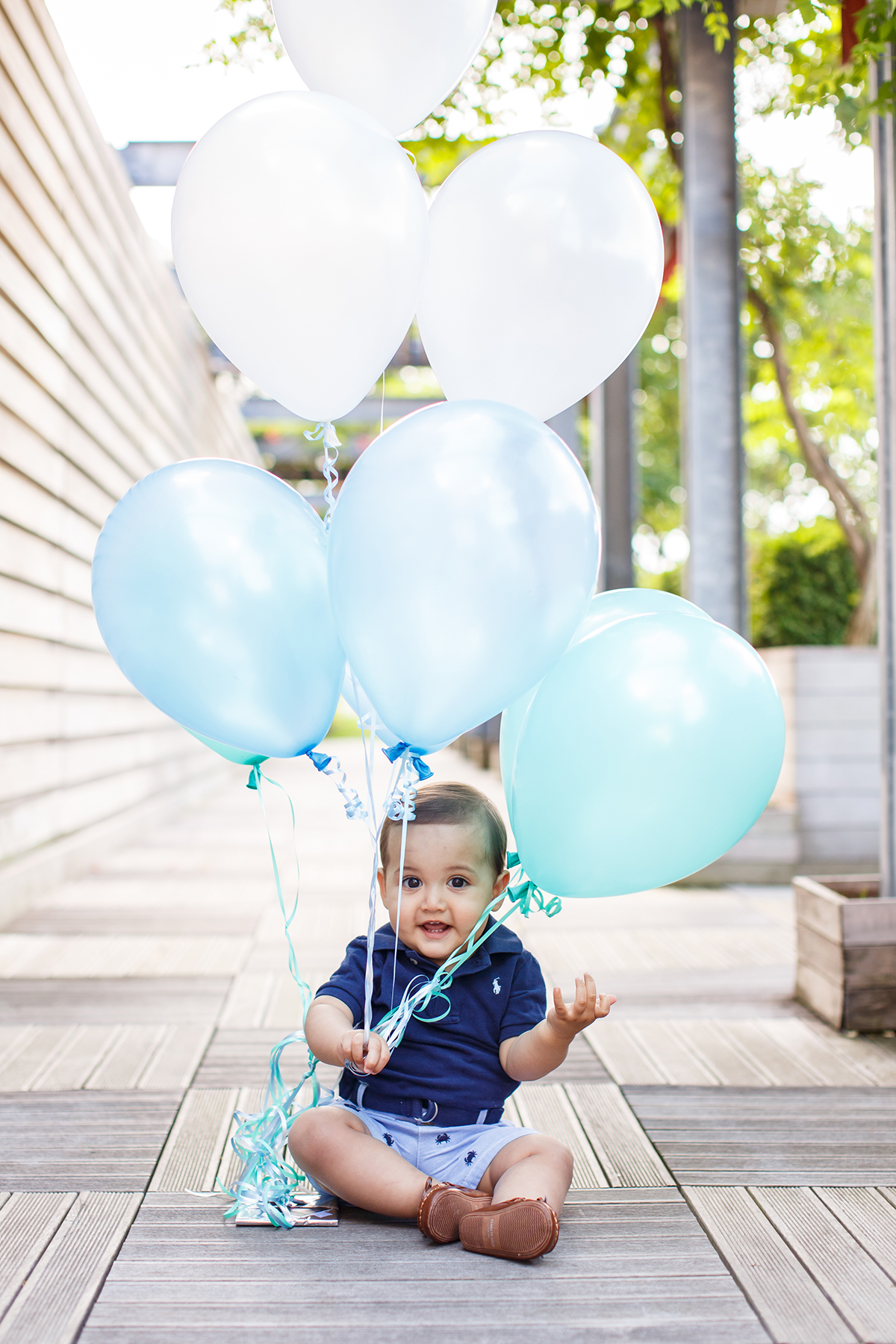 Close up of smiling toddler with white and blue balloons in his hand