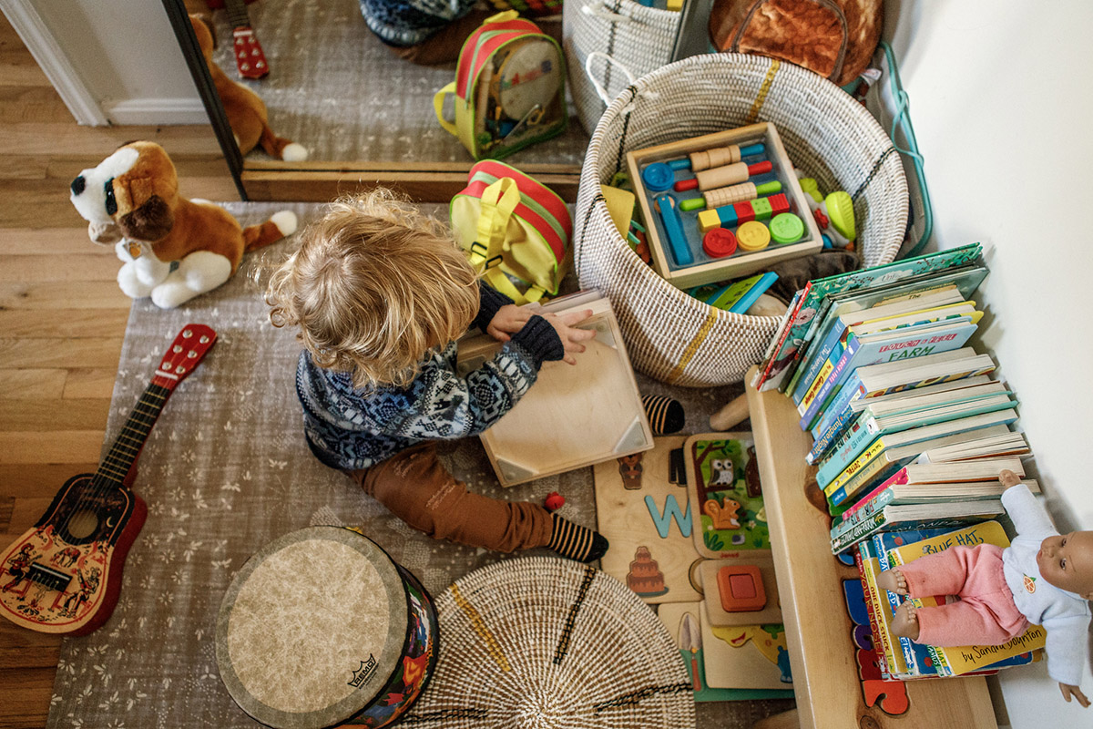 little boy in nursery reading all of his kids books surrounded by toys