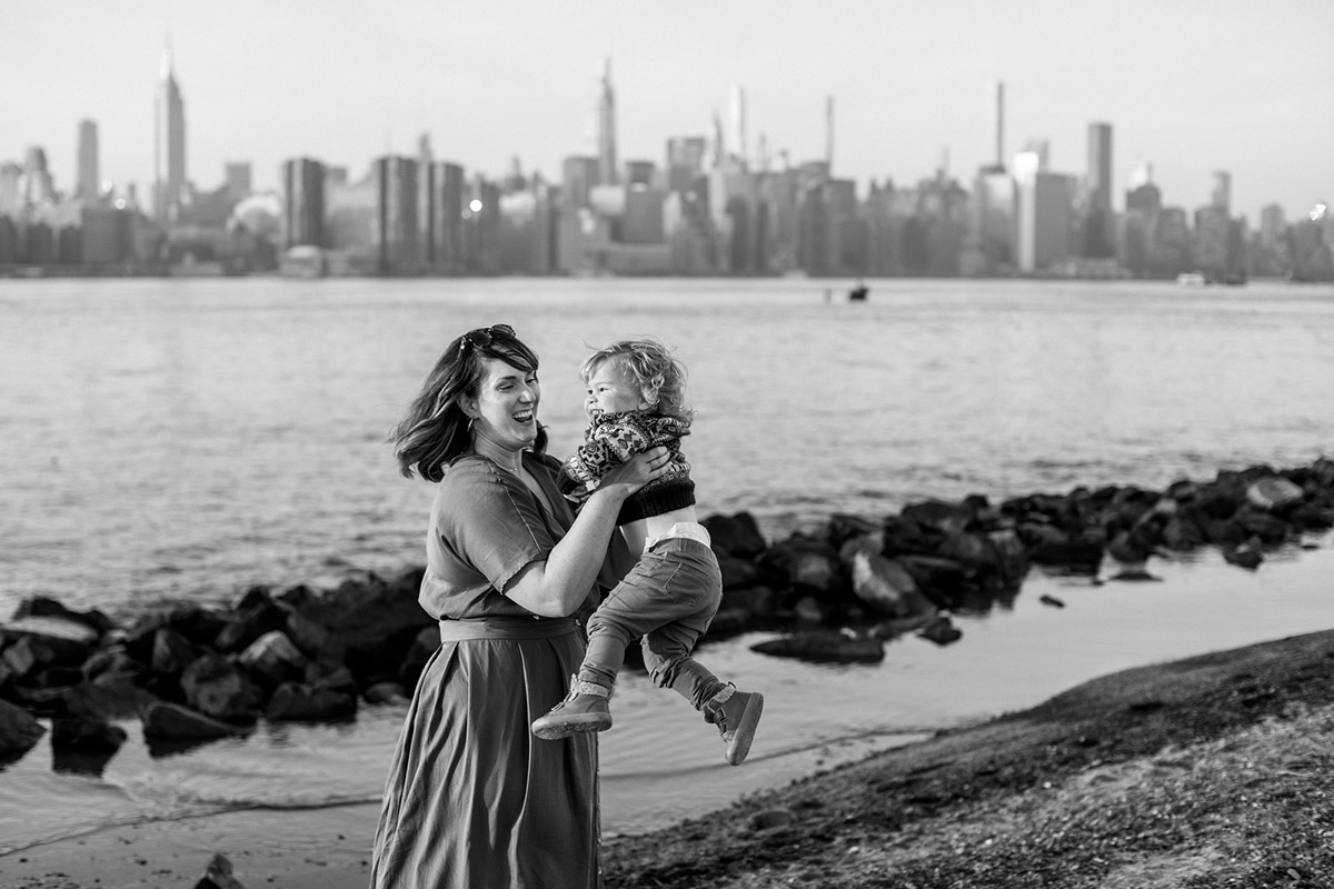 mom twirling her toddler boy around in dumbo with nyc skyline in the background