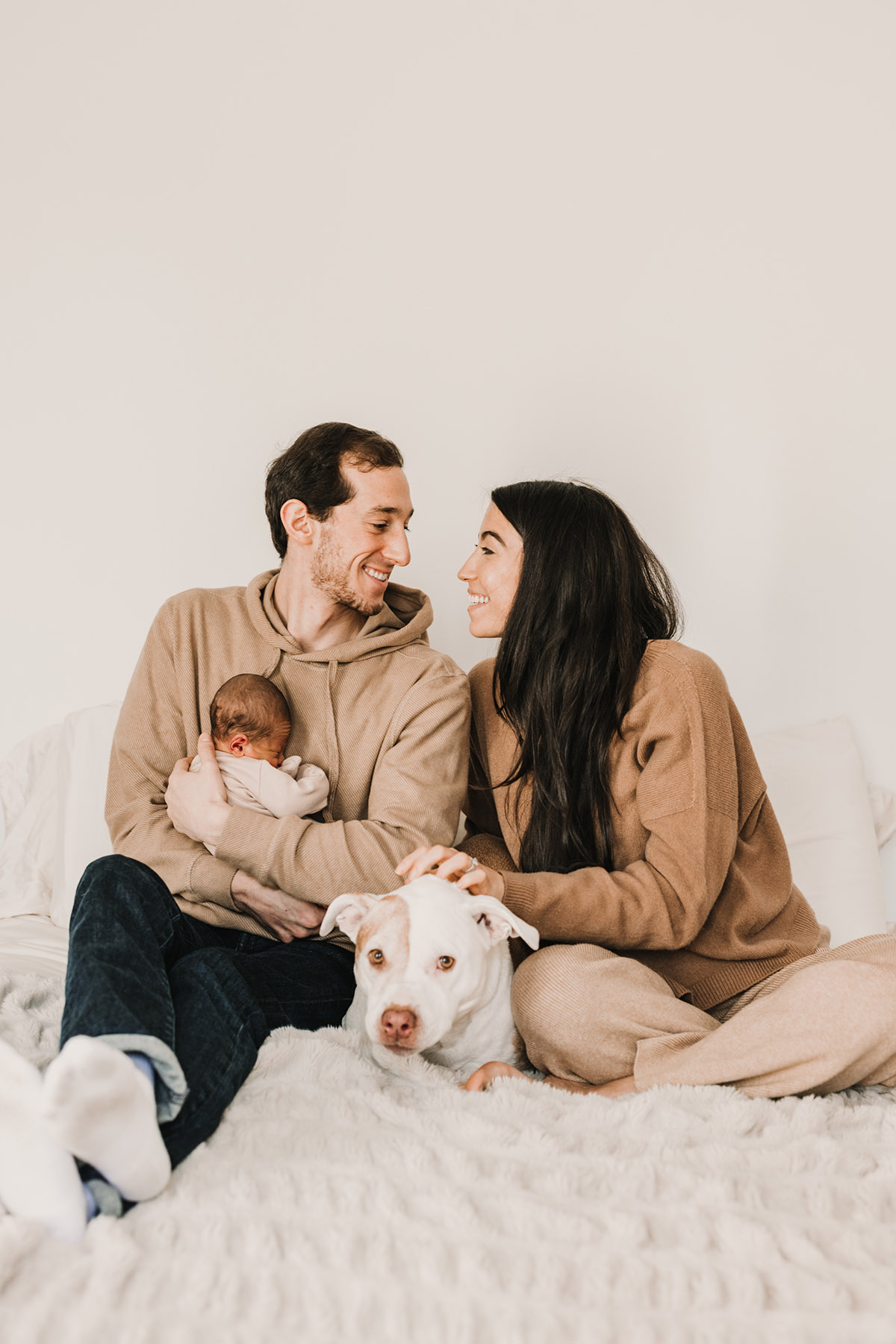 happy family with dog sitting on bed dad is holding newborn