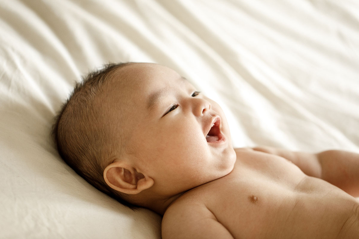 happy laughing baby on beige sheet sideview