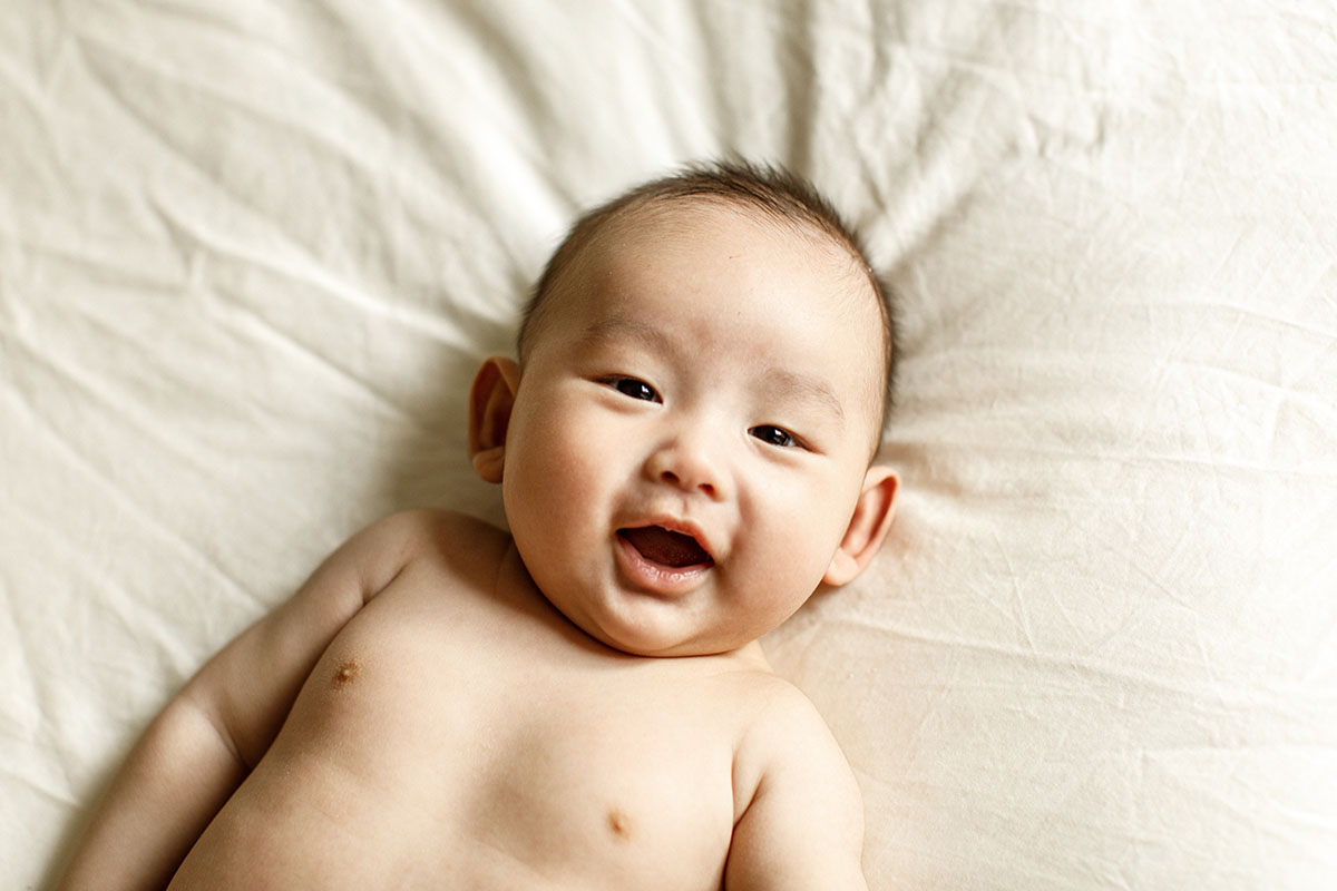 happy laughing baby on beige sheet frontview