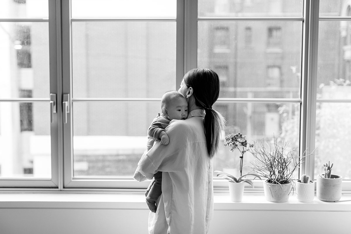 mom holding newborn in front of windows black and white