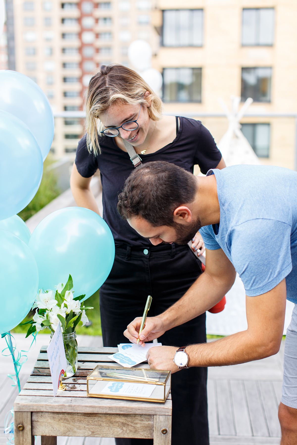 man and woman are signing a card in front of blue balloons