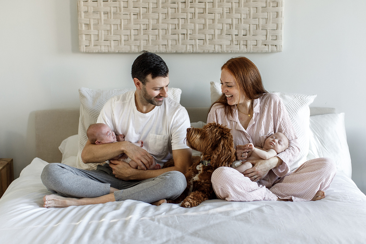 happy family with dog sitting on bed mom and dad holding their twin babies