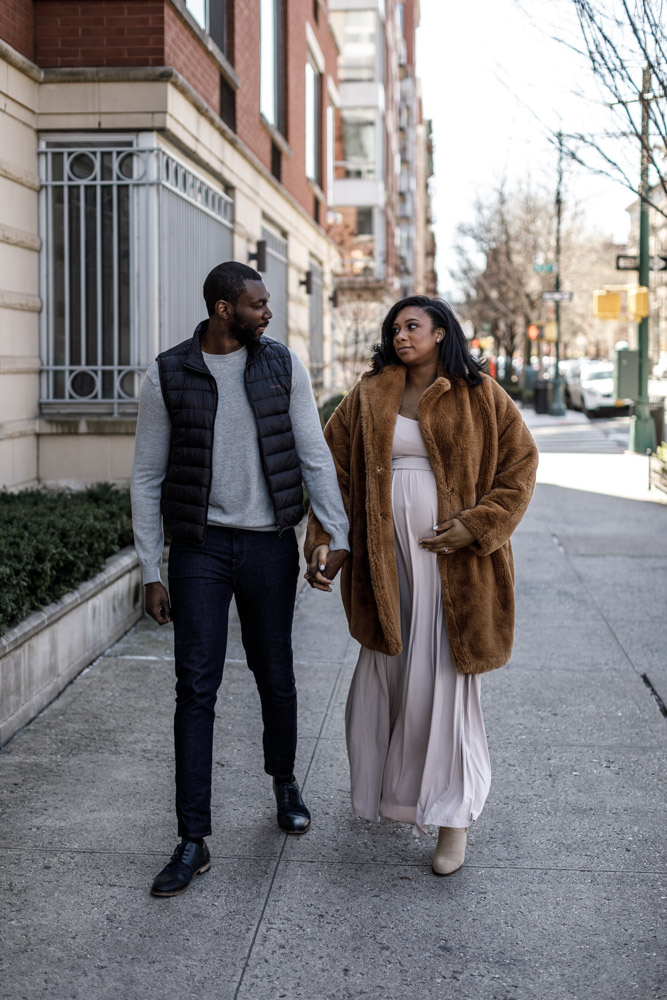 couple looking at each other as they walk down a street holding hands the woman is pregnant