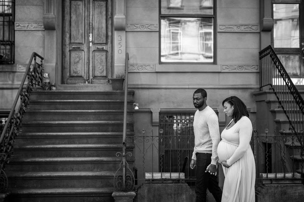 black and white photo of a couple walking down a street holding hands the woman is pregnant