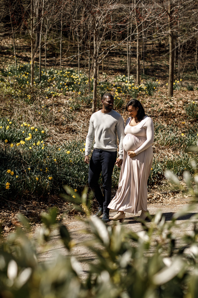 couple walking through a park holding hands the woman is pregnant