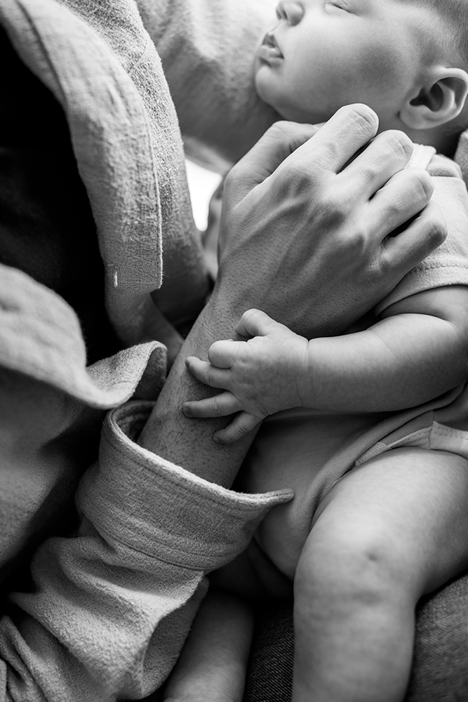 black and white photo of a baby laying in the lap of their parent