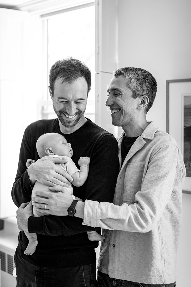 black and white photo of a couple holding their baby with big smiles on their faces
