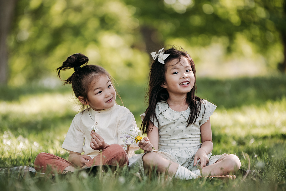 siblings sitting next to each other in a park both holding flowers