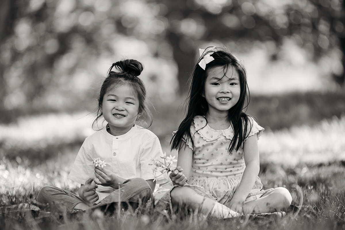 black and white photo siblings sitting next to each other in a park both holding flowers