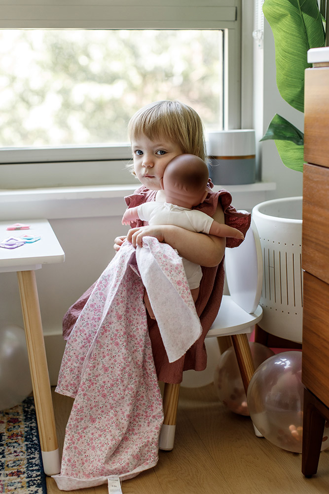 little girl hugging her baby doll in nursery