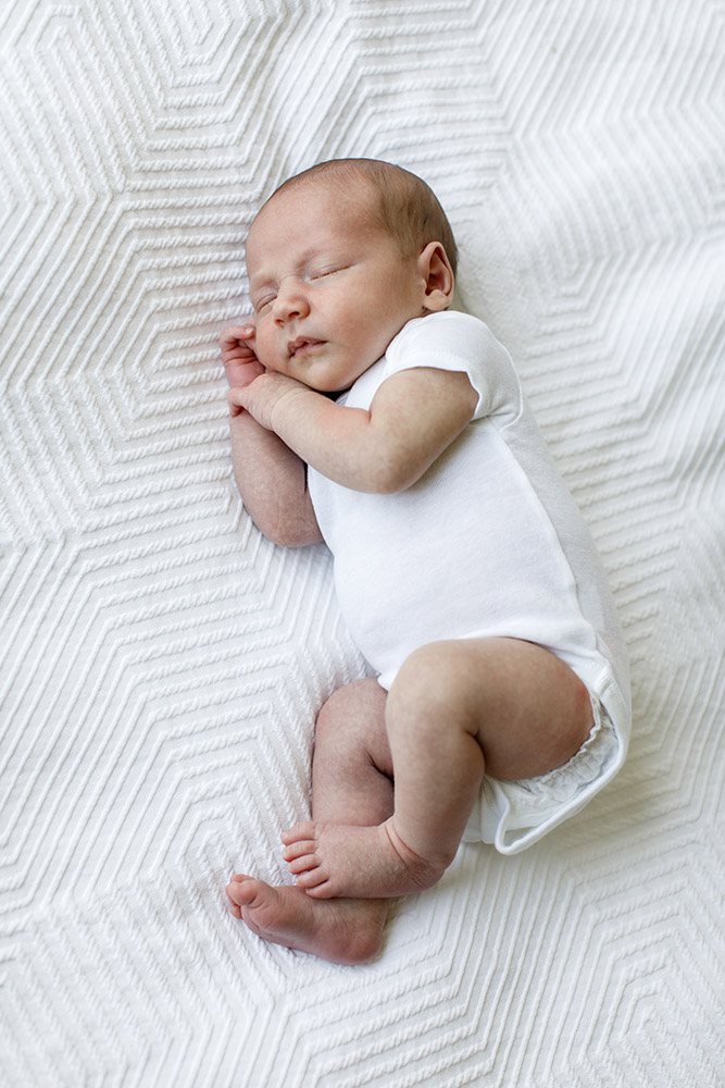 fully body portrait of sleeping newborn baby in white onesie