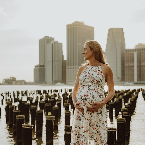 pregnant woman standing by the east river with new york skyline in the background