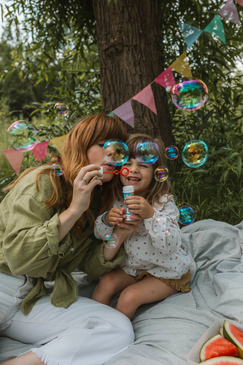 mom and daughter blowing bubbles on a picnic blanket
